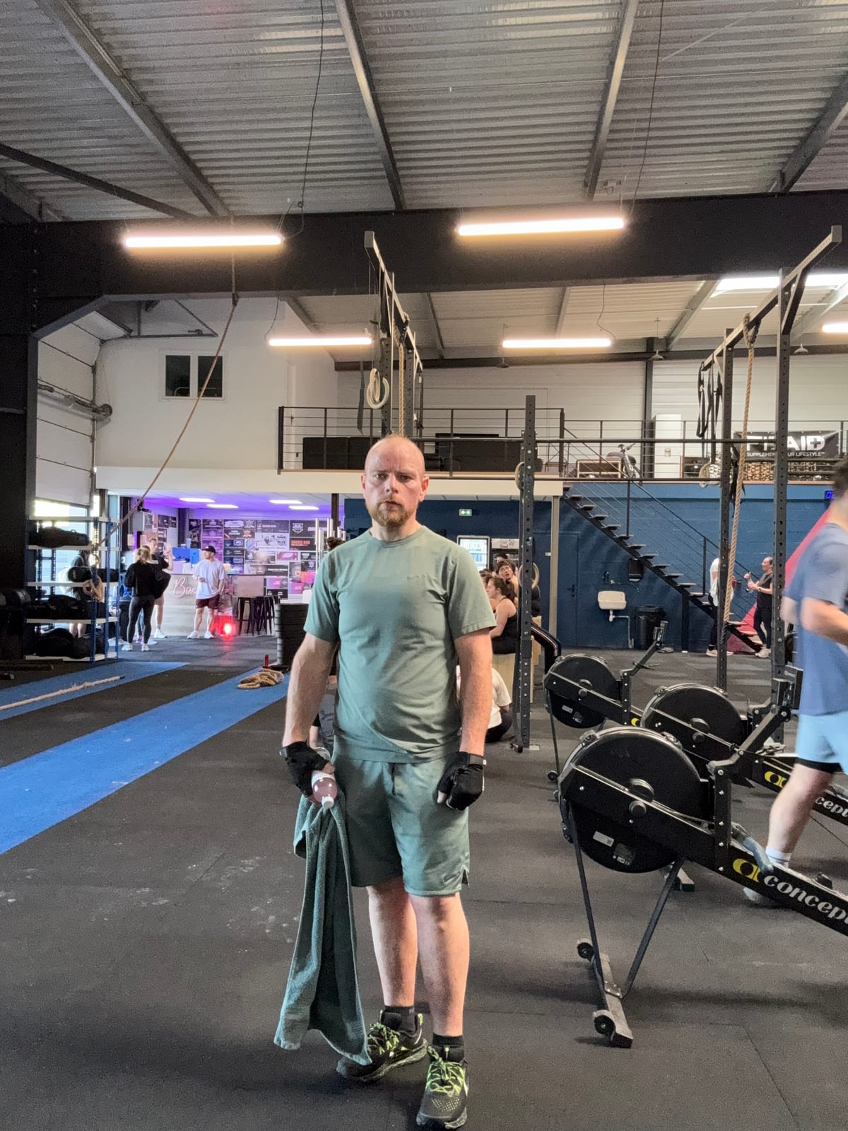 Bruno Mougenot debout dans la salle de CrossFit, rameurs et rig en arrière-plan